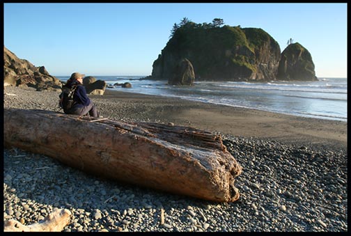 A woman hiker sits on a large driftwood log on Beach 3 in Olympic National Park
