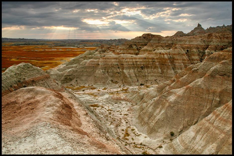 A dry and rocky valley with sun breaking through gray skies above, Badlands National Park, South Dakota and Psalm 23:4. valley of the shadow of death