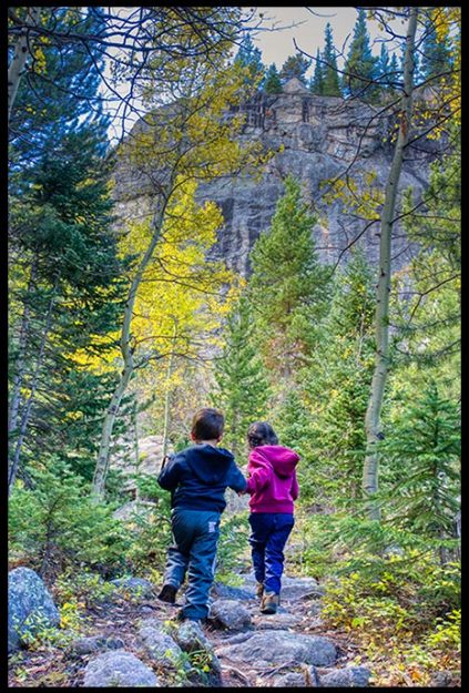 Children hike a trail toward yellow fall aspen trees near Mills Lake Trail, Rocky Mountain National Park, Colorado.