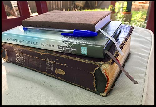 A stacked Bible, devotional journal and pen on a bench in a secret garden