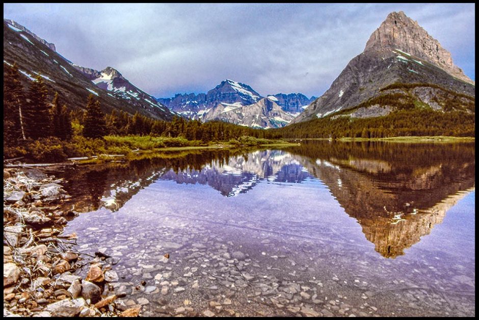  The surrounding mountains reflect off of Swift Current Lake in Glacier National Park, Montana. Bible verse of the day Luke 8:24 Jesus, the calm in the storm