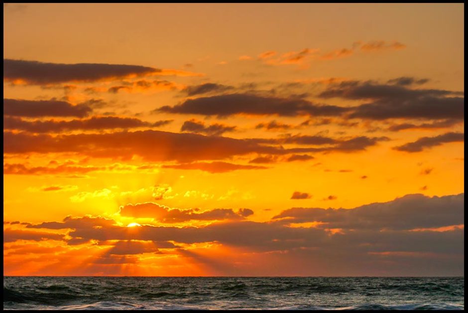 Sun beams break through clouds at sunrise over the Atlantic Ocean at Melbourne Beach, Florida and John 3:16-18. Bible Verse God so loved