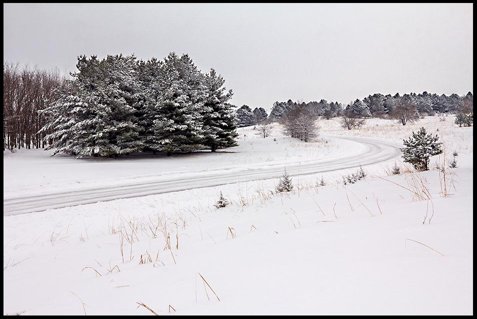 Snow-covered road curving through pine trees and small hills, Chalco Hills State Recreation Area, Nebraska. Isaiah 35:8Bible verse of the day and a highway of holiness