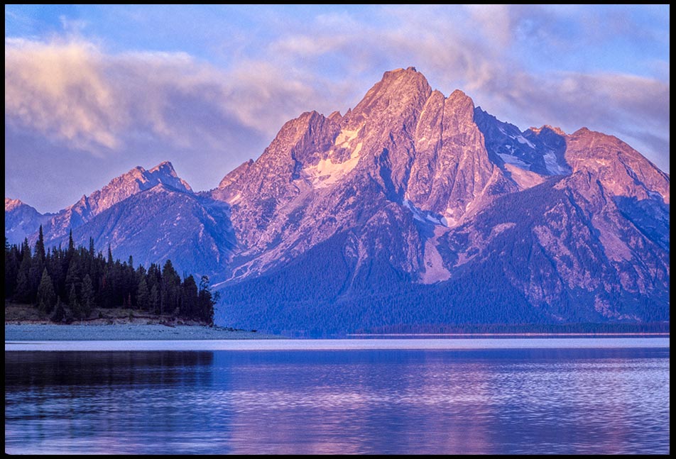 The alpine glow hits Mount Moran on the shore of Jackson Lake as seen from Coulter Bay, Grand Teton National Park. Bible verse 145:10-12, God’s Might acts