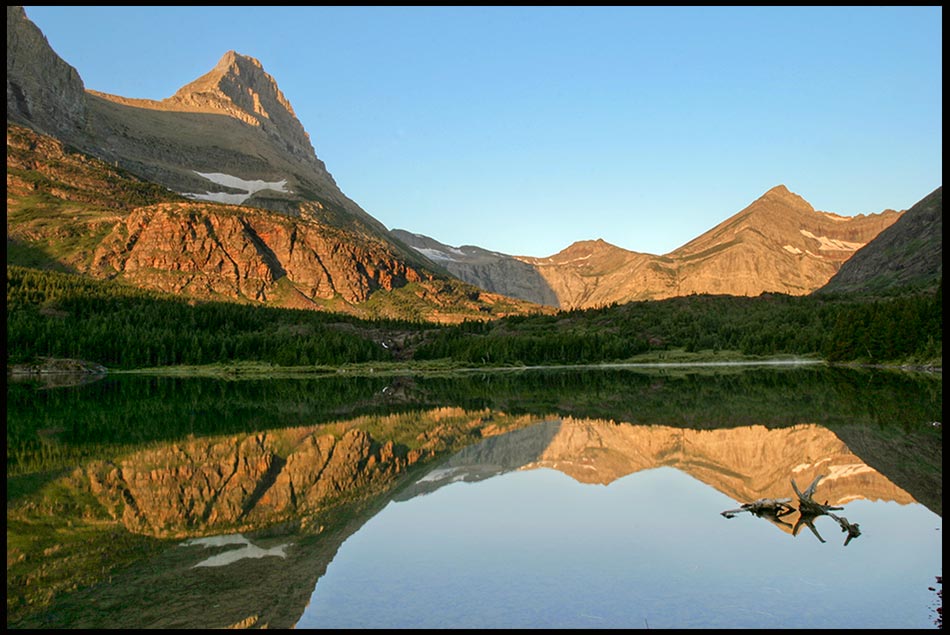 The flat water surface of Redrock Lake mirrors a reflection of the surrounding mountains in Glacier National Park, Montana and Psalm 117 Bible verse to Praise the Lord