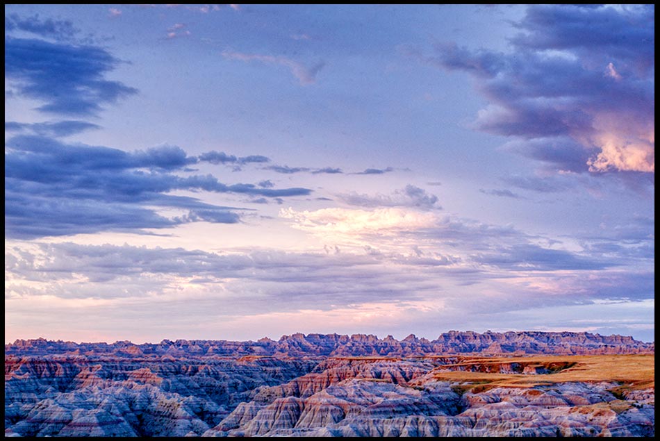 Blue, white and red clouds in the predawn sky over dessert rock formations in the Badlands National Park, South Dakota and Psalm 68:34. Bible verse about God strength in the skies
