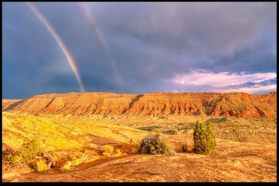 A Double Rainbow with grey sky and red rock and dirt landscape Arches National Park, Utah and Genesis 9:16-17 Bible Verse of the Day:
