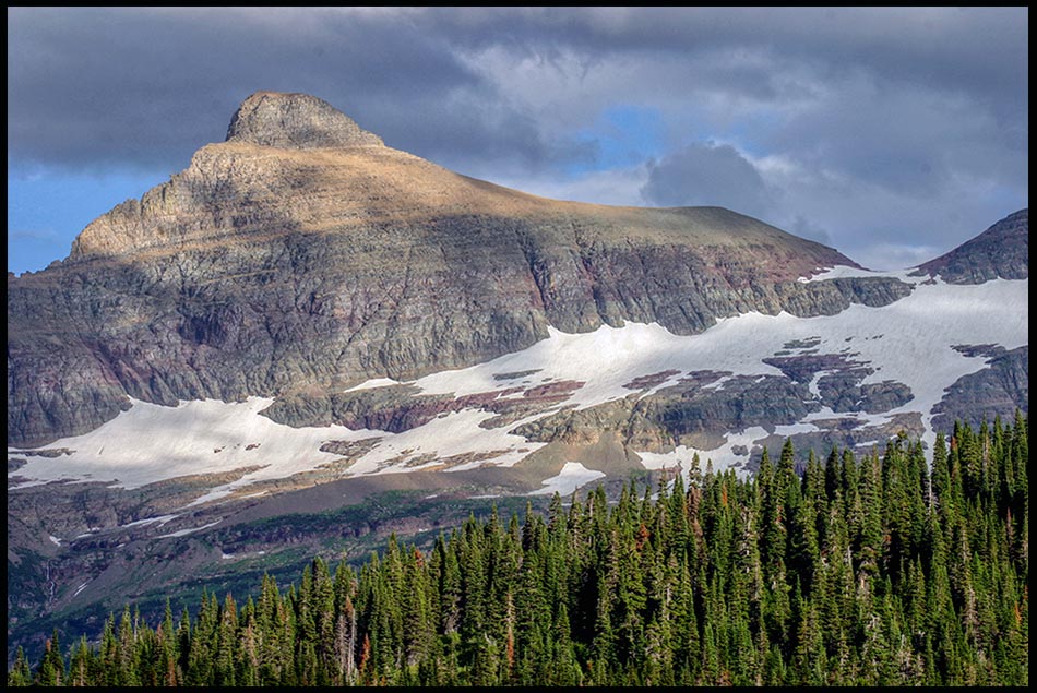 Sun clouds and snow on a mighty mountain peak Glacier National Park Montana and Bible Verse Psalm 68 16 on god's abode