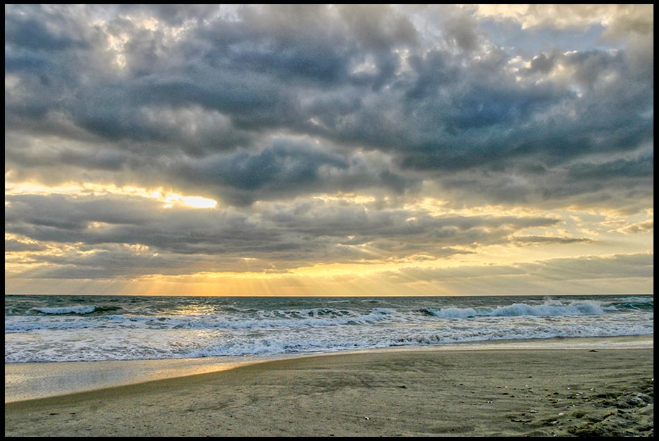 The Sun barley breaks through a mostly cloudy sky over white capped waves along the shore of Melbourne Beach Florida. Bible verse of the day the wind and the waves. Psalm 107:24–25
