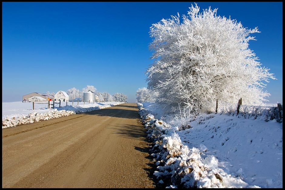 A rural dirt Road passing through snow and hoarfrost covered countryside under blue sky. Proverbs 16:17 Bible verse of the day: upright