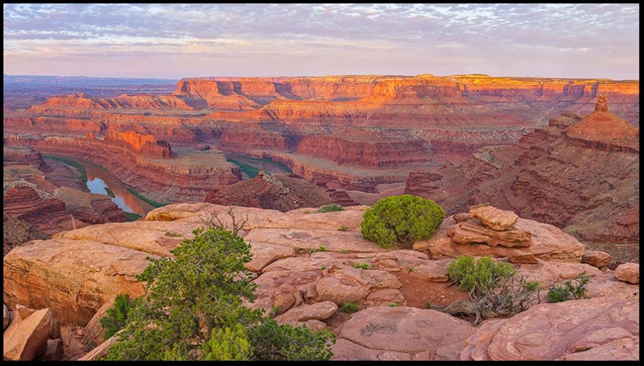 Bright green bushes sparsely top the cliffs Dead Horse Point, Utah in the early morning light. Bible verse of the day Psalm 113:3 