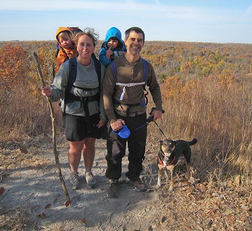 A man and a woman hiking on the hilltop with two children and backpacks and with their dog in autumn. All in relationship
