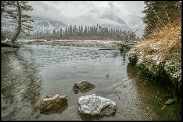 Rocks in slow moving river surrounded cloud covered Canadian Rockies in winter, Alberta, Canada. Psalm 46:4-5 Bible verse God in our Midst