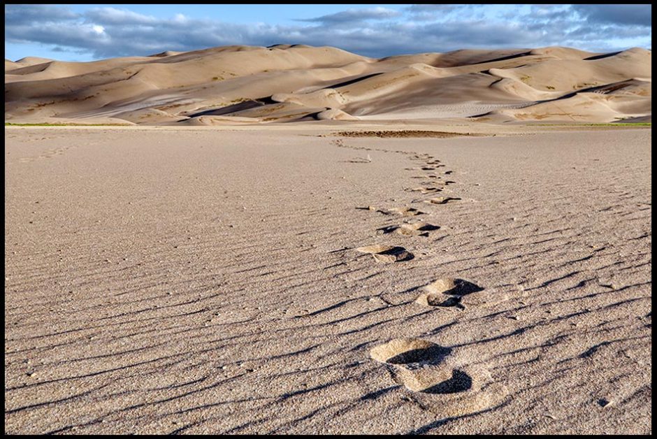 Footsteps reaching out across a flat sandy area headed towards sand dunes, in Great Sand dunes National Park, Colorado. Bible verse of the day and nature photo Psalm 17